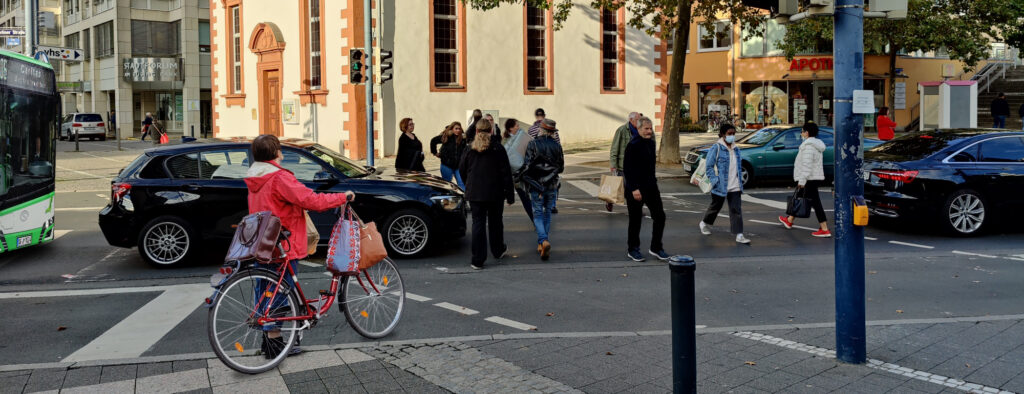 Ampel an der Berliner Straße, Auto auf dem Fußgängerüberweg, Fußgänger zwischen Autos, Radfahrerin, Bus